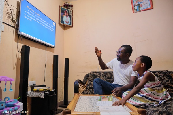 ノートを見ながらテレビ授業を受けるデボラさん(10歳)。理解を助けるため、父親が説明している。(ガーナ、2020年3月撮影) © UNICEF_UNI342096_
