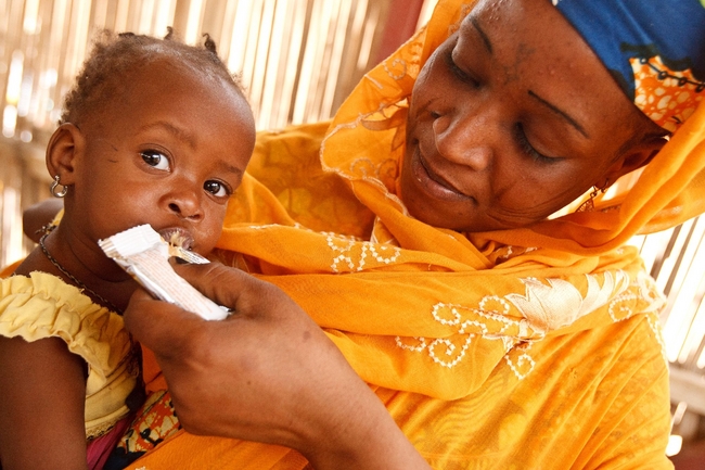 子どもに栄養補助食品（プランピーナッツ）をあげる母親（ニジェール） ©UNICEFNYHQ2012-0180OLIVIER ASSELIN