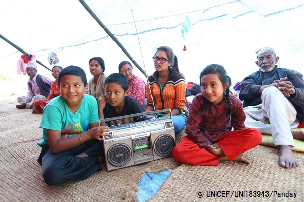 大地震が起こったネパールで、避難所のテントに集まってユニセフが支援するプログラムを聞く子どもたちや家族。© UNICEF_UNI183943_Panday