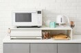 オリジナルキッチンブランドtesione（テシオン）から、幅48〜90cmまで伸縮できる家電下スライドテーブルを新発売。電子レンジや炊飯器の下を有効活用し、収納と"ちょい置き"を両立。