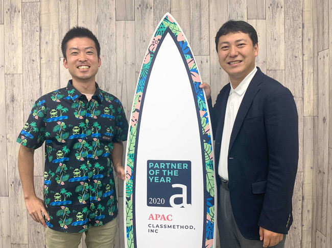 受賞記念サーフボードと、当社代表の横田聡（写真右）、データアナリティクス事業本部マネージャーの大場裕喜（写真左）