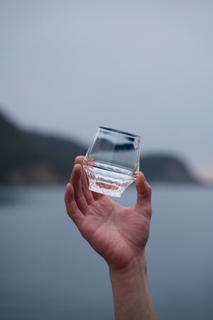 画像の説明：海を背景にKINJO JAPAN F0（通称：SAKEグラス）を掲げているカット