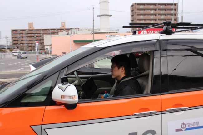 写真２：運転席が無人の自動運転車の助手席で本学大学院生がシステム監視者を担当