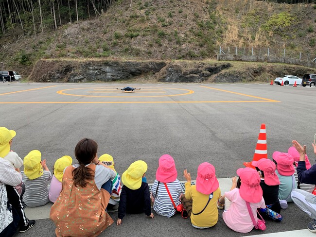 地元シイタケを搭載した物流専用ドローン”AirTruck”の着陸を見守る佐那河内村の保育園児 (佐那河内村役場駐車場) 地元シイタケを搭載した物流専用ドローン”AirTruck”の着陸を見守る佐那河内村の保育園児 (佐那河内村役場駐車場)