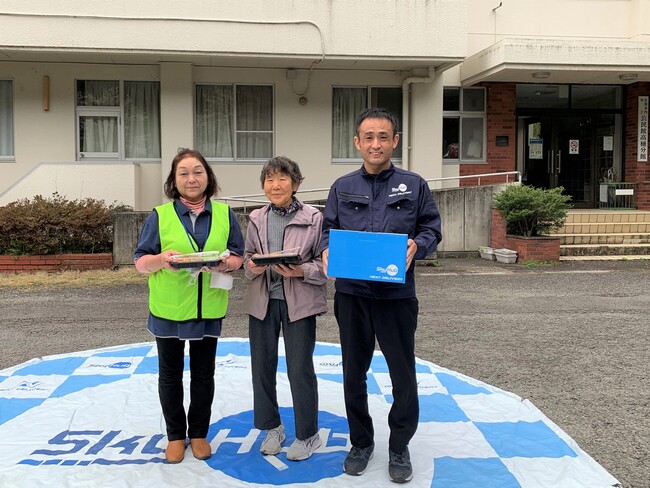 日本発物流専用ドローン“AirTruck”で配送された2人分のお弁当とお茶を受け取った住民と記念撮影 日本発物流専用ドローン“AirTruck”で配送された2人分のお弁当とお茶を受け取った住民と記念撮影