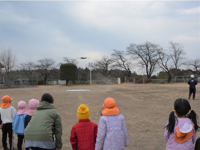 ドローンの着陸を見守る近所の保育園児たち（仮ドローンデポ：旧九十九小学校グラウンド）