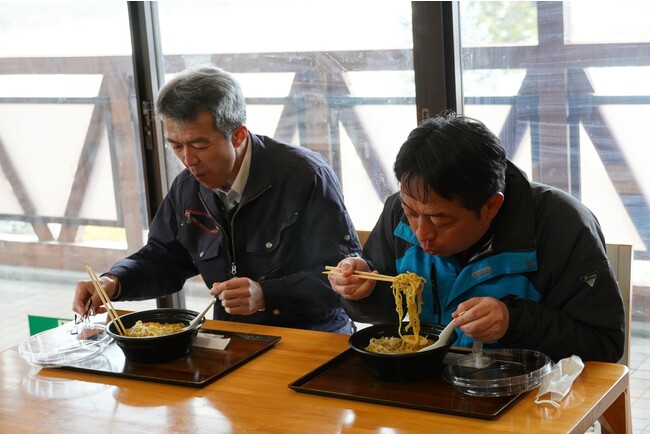 ドローン配送されたラーメンを食べる 佐々木執行役員(岩泉HD)と 箱石さん(ふれあいらんど館長) (ふれあいらんど内センターハウスにて) ドローン配送されたラーメンを食べる 佐々木執行役員(岩泉HD)と 箱石さん(ふれあいらんど館長) (ふれあいらんど内センターハウスにて)