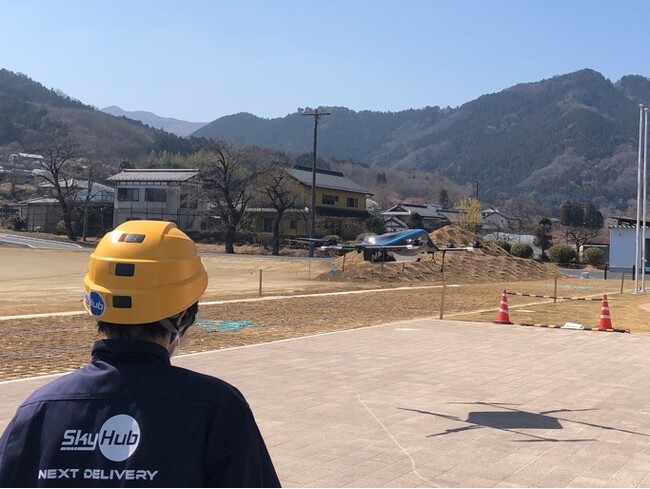 サイクリストのお土産を載せた復路飛行をするドローンの着陸を見守るスタッフ (神川町多目的交流施設) サイクリストのお土産を載せた復路飛行をするドローンの着陸を見守るスタッフ (神川町多目的交流施設)