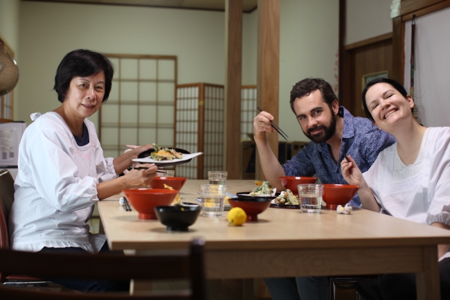 浅草在住のホスト、内山さん宅で、初めて作った天ぷらとうどんにご満悦の表情を浮かべる台湾からの旅行者ウェンディ（左）とイタリア人カップル、ダニエルとイレーネ(右)