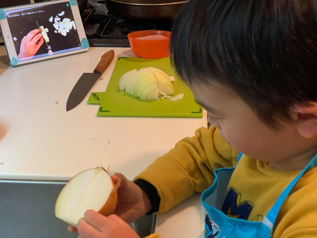 FamCookの子手伝い機能で玉ねぎの皮をむく男の子。パパの料理塾で学んだ料理を親子で復習中。