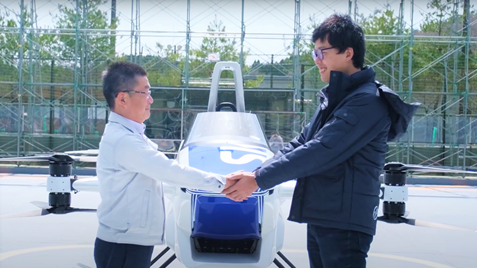 SkyDrive「空飛ぶクルマ」の前で握手する 三栄工業 代表取締役社長 神谷（左）とSkyDrive 代表取締役CEO 福澤（右）