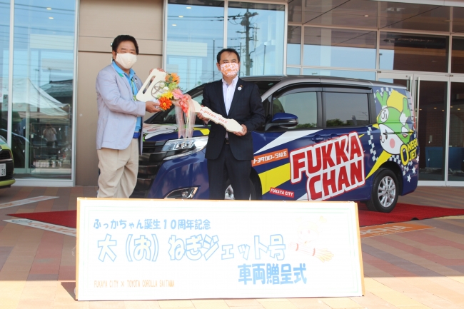 茂木（もぎ）副社長（写真右）から小島（こじま）市長に車両レプリカキー贈呈