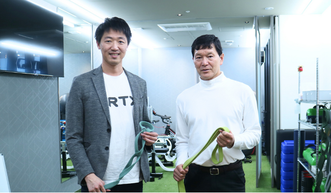 【写真】左) 当社代表取締役 ビクターチン 右) VRTXの顧問に就任した山本利春氏