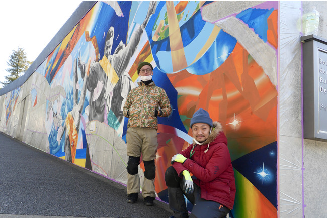 壁画の政治セクションの前に立つアーティストユニット「WHOLE9」のhitch氏とsimo氏