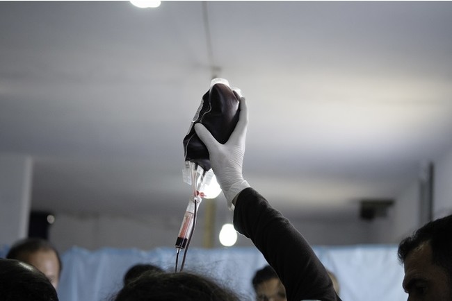 イドリブ県の農場を改造して作ったMSFの仮設病院で、血液バッグを掲げる医療スタッフ＝2013年7月22日　(C) Robin Meldrum／MSF