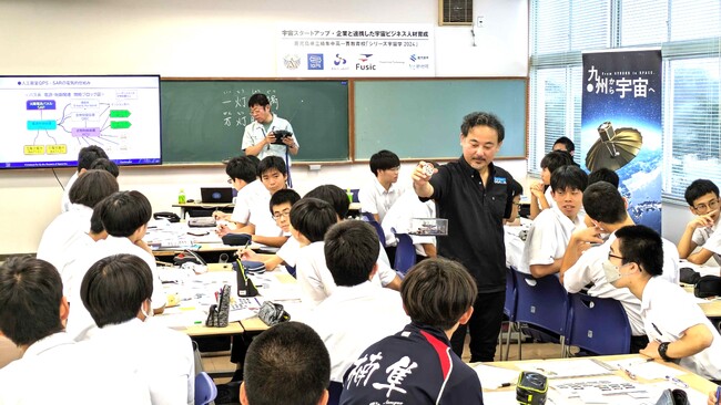 衛星開発のバス系を担当する昭和電気研究所の古賀主幹技師は、衛星に搭載される機器「リアクションホイール」について、その原理を模型を使って説明。