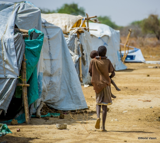 南スーダン国内の避難民キャンプで、幼い妹を抱いて歩く少年