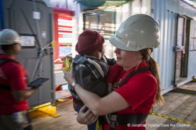 地中海で救助された子どもを抱きかかえるセーブ・ザ・チルドレンのスタッフ