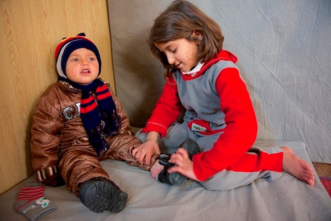 © UNICEF Jordan/2013/Shehzad Noorani  9歳のアヤちゃんが、２歳の妹にユニセフが支援した防寒着を着せてあげています。