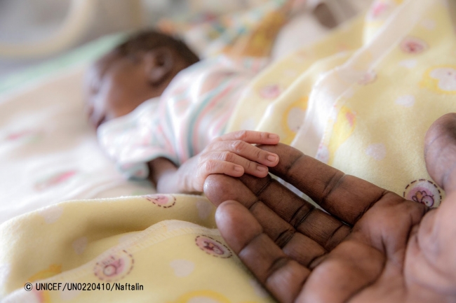 南スーダンのジュバにある病院で、わずか1300グラムで生まれ、保育器に入っている赤ちゃん。母親は分娩時の出血が原因で亡くなった。見守っている祖母が、赤ちゃんの小さな手にそっと触れている。© UNICEF_UN0220410_Naftalin