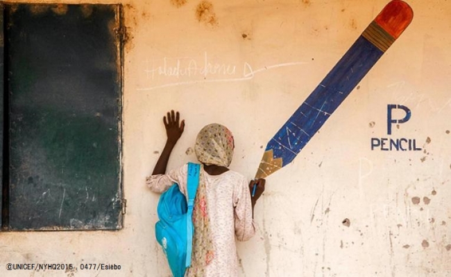国内避難民キャンプの壁に描かれた鉛筆の前で、ポーズをとる13歳のアイシャさん。(ナイジェリア・アダマワ州) (C)UNICEF_NYHQ2015-0477_Esiebo