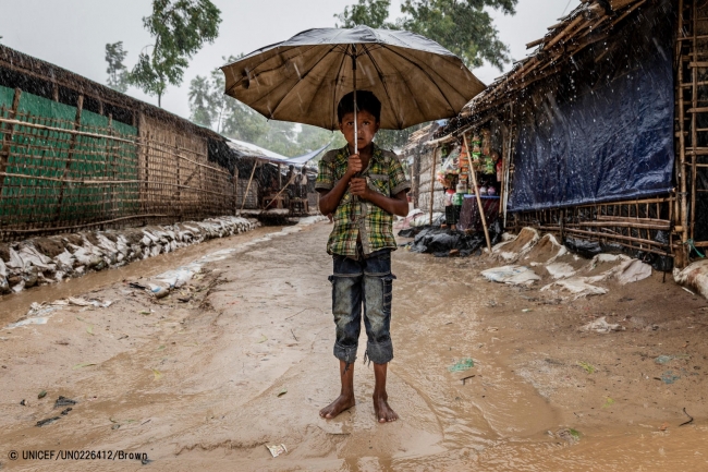 モンスーン期の雨で水が溢れる道に、裸足で立つ難民の男の子。(2018年7月撮影) (C) UNICEF_UN0226412_Brown
