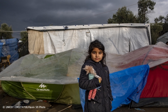 ギリシャのレスボス島モリアにある難民・移民受入・身元確認センターで、滞在するテントの前に立つ女の子。(2018年12月撮影) (C) UNICEF_UN0274758_Haviv VII Photo