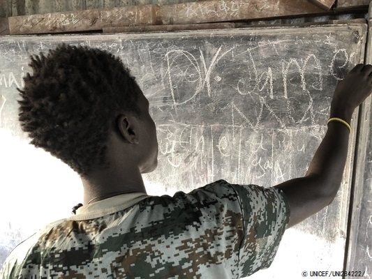 「子どもにやさしい空間」の黒板の前に立ち、「平和」の文字を指さす元子ども兵士のジェームスさん(仮名)。(2020年1月撮影) © UNICEF_UNI284222_