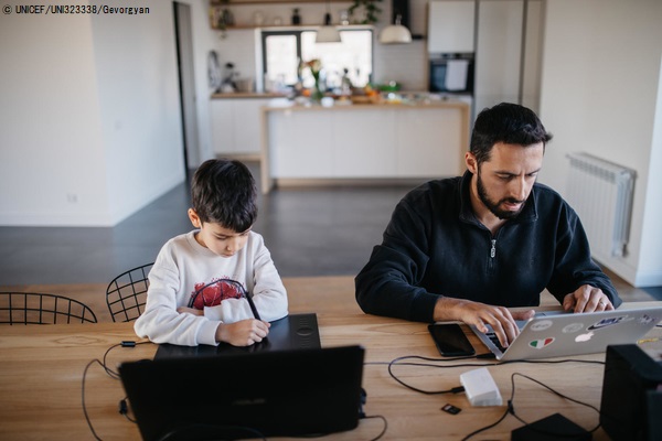 自宅で仕事をする父親の隣で、パソコンを使って遠隔授業を受ける7歳のダニーくん。(アルメニア、2020年4月14日撮影) © UNICEF_UNI323338_Gevorgyan