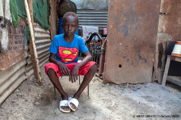 マラカルの文民保護区(Protection of Civilians (PoC) Site)の自宅前に座る10歳のチョギくん。ユニセフの支援で5年離れ離れだった母親と再会することができた。(2020年10月撮影) © UNICEF_UN0475217_Na