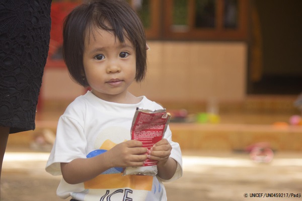 東ヌサ・トゥンガラ州の自宅で、すぐに食べられる栄養治療食(RUTF)を手に持つ、重度の消耗症と診断された1歳のフェリシティちゃん。(インドネシア、2021年2月撮影) © UNICEF_UN0459217_Padji