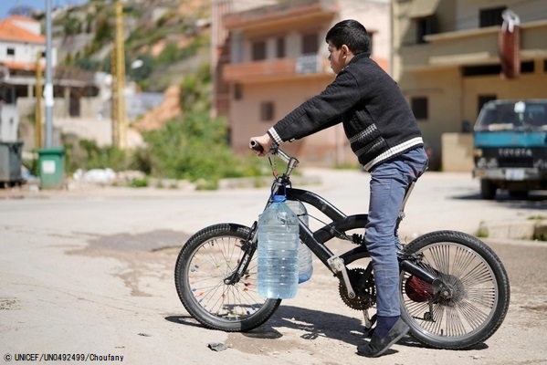 6リットルの容器2つに水を汲み、自転車で家に向かう11歳のアドハムくん。(2021年3月撮影) © UNICEF_UN0492499_Choufany