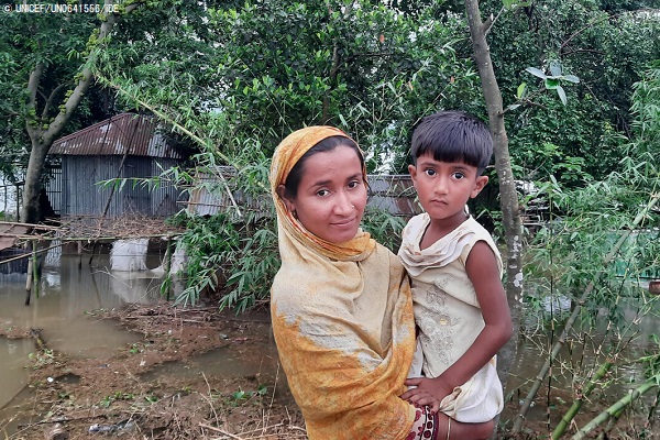 洪水で水浸しになり壊れてしまった家の前に立つ親子。母親のラクサナさんは「食料が手に入るかどうか不安です。ここにはトイレも飲み水もありません」と話す。(バングラデシュ、2022年5月16日撮影)(C) UNICEF_UN0641556_