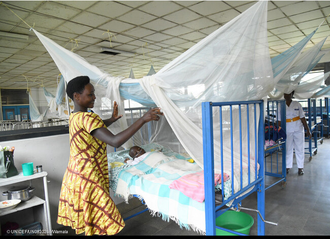 病院の小児科病棟で入院している赤ちゃんのベッドに、マラリア感染を予防するため蚊帳をかける母親。(ウガンダ、2023年4月撮影) (C) UNICEF_UN0832246_Wamala