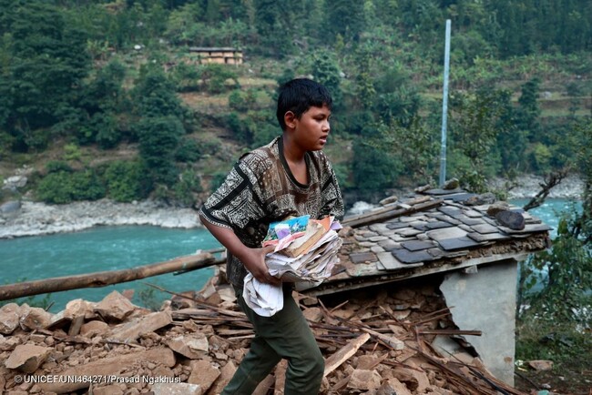 西ルクム郡で、地震により全壊した自宅から家財道具を運ぶ12歳のダーンラさん。「がれきになった家の中から本を数冊は取り出せた。学校にはいつ戻れるんだろう」と話す。(ネパール、2023年11月6日撮影) (C) UNICEF_UNI464271_Prasad Ng