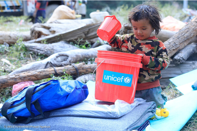 地震の被害が最も甚大だった地域のひとつ、ルクム西部のAathbiskotに届けられた、防水シートや毛布、衛生キットなどを含むユニセフの支援物資を受け取った子ども。(ネパール、2023年11月6日撮影) (C) UNICEF_UNI465093_Prasad N