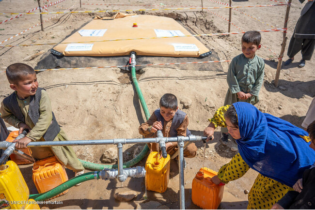 西部ゴール州で、ユニセフの支援により届いた安全な水を汲む子どもたち。ユニセフは5000リットルの水を貯水袋に供給し、毛布や子ども服、バケツ、給水タンク、石けん、浄水剤などの衛生物資を被災した家族に届けた。(アフガニスタン、2024年5月28日撮影) (C) U