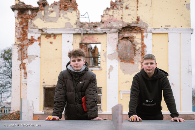 ハルキウの破壊された学校の前に立つステパンさん(右・15歳)とヤロスラフさん(左・16歳)。オンライン授業を受けているが、電力不足でネットが使えないこともある。(ウクライナ、2023年12月撮影) (C) UNICEF_UNI510560_Pashkina