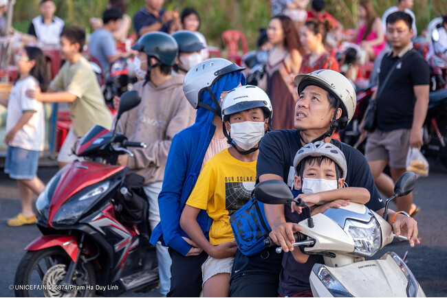 ホーチミンで、マスクを着用してバイクに同乗する子どもたち。ベトナムでは、老朽化した自動車の排気ガスや、石炭発電、廃棄物処理による大気汚染が課題になっている。(ベトナム、2024年4月撮影) (C) UNICEF_UNI565874_Pham Ha Duy Li