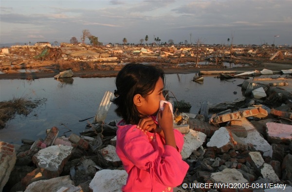 スマトラ沖地震・津波の災害後、バンダ・アチェ郊外の自宅があったあたりで立ち尽くす女の子。鼻を覆わなければならないほど、臭気が漂っていた(2005年、インドネシア) © UNICEF/NYHQ2005-0341/Estey