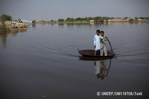 洪水の水が引かない中、大きな鍋を使って移動する子ども。（パキスタン、2011年撮影）© UNICEF_UNI116709_Zaidi