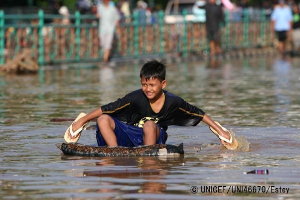 洪水の水が引かないなか、漂流物に乗り、サンダルをペダルにして移動する男の子。（インドネシア、2007年撮影）© UNICEF_UNI46670_Estey