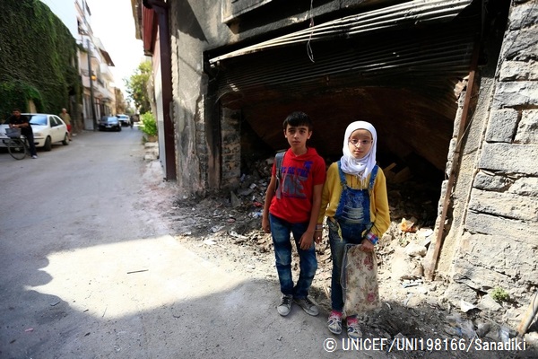 荒廃した建物の近くに立つホムス旧市街出身の12歳の双子。（シリア）© UNICEF_UNI198166_Sanadiki