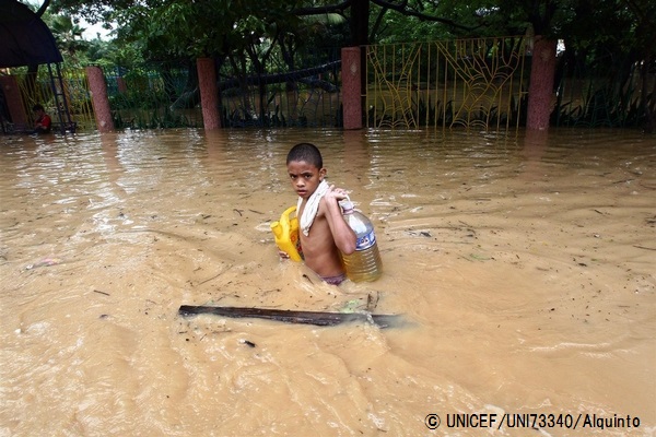 洪水の水が引かない中、給水タンクを抱えて歩く男の子。（フィリピン）© UNICEF_UNI73340_Alquinto