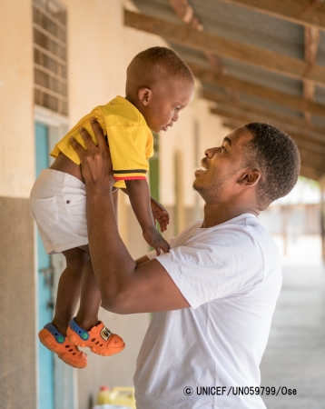 生後1歳10カ月の息子を抱き上げるお父さん（ウガンダ）。© UNICEF_UN059799_Ose