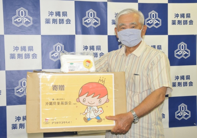 アリカワコウヘイ！から寄贈されたマスクを持つ沖縄県薬剤師会の亀谷浩昌会長。