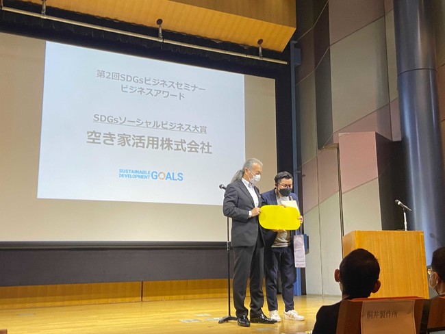 表彰式で会社のロゴを手に記念撮影する、空き家活用株式会社代表、和田 貴充（右）