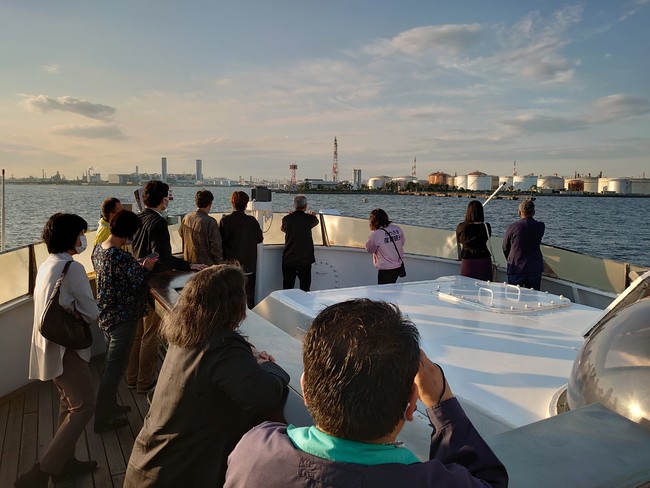 往路：川崎港内にてガイドより説明。屋上デッキから360度遮るもののないデッキから港の景色を楽しんでいただきました