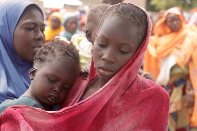 ボコ・ハラムによる脅威で食糧不安が続くナイジェリア。色鮮やかな服装とは裏腹に、疲れきった表情で、生きるために欠かせない国連WFPの食糧配給を受け取りにやってくる親子。WFP Amadou Baraze