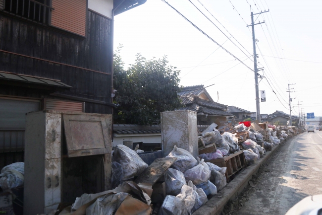 住宅の前に整然と積まれた、泥をかぶった家財道具の数々（7月14日、岡山県）